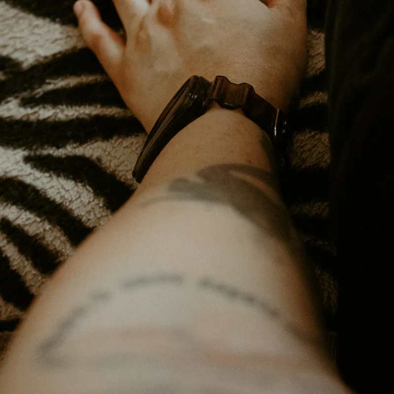 Avant-bras d'homme avec une montre et un petit tatouage en lettrage fin près du poignet