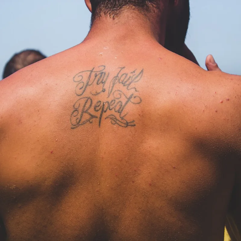 Petit tatouage en lettrage entre les omoplates d'un homme, zone couverte par une chemise